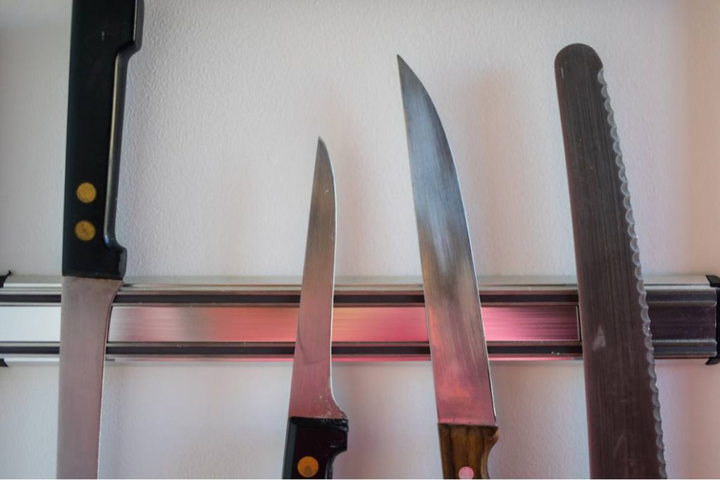A set of chef's knives magnetically attached to a wall-mounted strip in a kitchen.